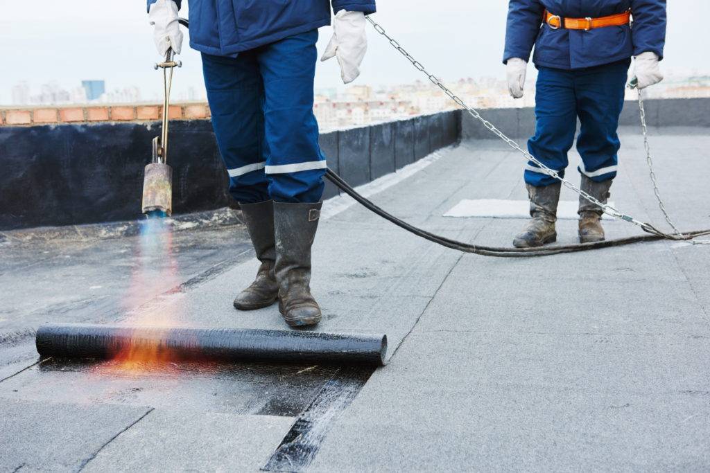 Heating and melting bitumen roofing felt by flame torch